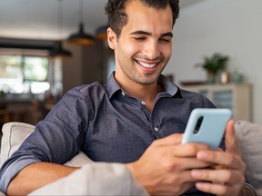 Happy man using smartphone while sitting on sofa at home.