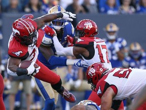 Calgary Stampeders RB Ka'Deem Carey (centre) is sent flying by Blue Bombers DT Casey Sayles during CFL action at IG Field in Winnipeg on Sunday.