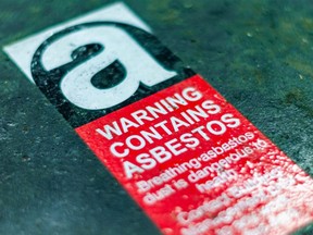 A bright red sticker sign warns of asbestos on a rusting material