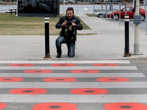 Veteran Andy Sinclair, who served 29 years as a flight engineer with the Canadian Forces, takes a photo of a crosswalk painted with poppy's in Chestermere. Sinclair is happy to see the crosswalk but the Legion says people walking over the poppy's is disrespectful and wants to see the poppy's removed. Friday, October 22, 2021. Brendan Miller/Postmedia