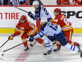 The Calgary Flames’ Dillon Dube, left, and Andrew Mangiapane battle the Winnipeg Jets’ Jansen Harkins, left, and Dominic Toninato for the puck during NHL pre-season action at the Scotiabank Saddledome in Calgary on Friday, Oct. 8, 2021.