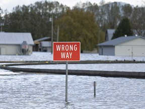 A road sign is surrounded by flood waters as a farm is pictured in the background in Chilliwack, B.C., Tuesday, November 16, 2021.
