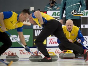 Ben Hebert (left) and B.J. Neufeld brush a rock into the house as skip Kevin Koe sits in the house during a game at the Tim Hortons Brier at the Markin MacPhail Centre at Canada Olympic Park in Calgary on March 13, 2021.