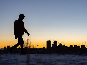 A pedestrian walks on a pathway as the sun sets behind the Calgary skyline on a cold day on Monday, December 6, 2021.