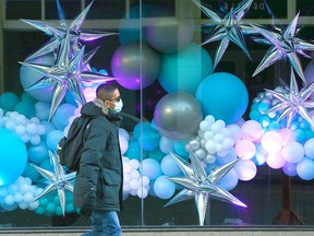 A pedestrian wearing a face mask walks on 1 St. SW between Stephen Ave. and 9 Ave. SW and passes a festively decorated window in downtown Calgary on Sunday, December 12, 2021.