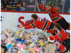 Calgary Hitmen Cael Zimmerman, top, Tyson Galloway and Adam Kidd dive into teddy bears after Zimmerman scored the first goal against the Lethbridge Hurricanes during the Hitmen’s Teddy Bear Toss game at the Scotiabank Saddledome in Calgary on Saturday, Dec. 4, 2021.