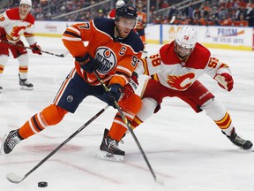 Edmonton Oilers forward Connor McDavid (left) tries to carry the puck around Calgary Flames defencemen Oliver Kylington at Rogers Place in Edmonton on Saturday, Jan. 22, 2022.