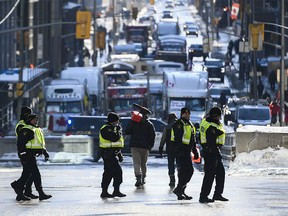 A protester carrying an empty fuel container on a broom handle walks on Metcalfe Street past Ontario Provincial Police officers, as a protest against COVID-19 restrictions that has been marked by gridlock and the sound of truck horns continues into its second week in Ottawa on Monday, Feb. 7, 2022.