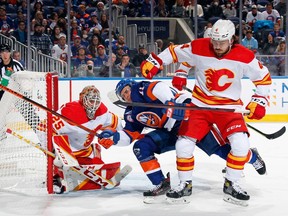 Goaltender Jacob Markstrom and Rasmus Andersson of the Calgary Flames defend against Zach Parise of the New York Islanders at UBS Arena in Elmont, N.Y., on Nov. 20, 2021.
