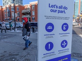 Masked pedestrians walk by a COVID-19 safety sign outside the Best Buy on 17th Avenue S.W. on Thursday, Feb. 3, 2022.