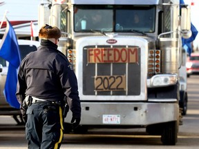 An RCMP officer monitors a blockade of trucks and other vehicles about 15 kilometres north of the border crossing at Coutts, Alta., on Feb. 8, 2022.