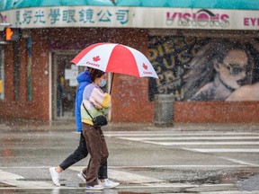 Two pedestrian take shelter under an umbrella as they cross a street in Calgary's Chinatown on a snowy day on Tuesday, April 19, 2022.