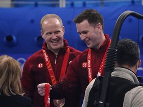 Canada’s Brad Gushue, right, looks at a bronze medal with teammate Mark Nichols by his side, at the Beijing Winter Olympics on Feb. 19, 2022.