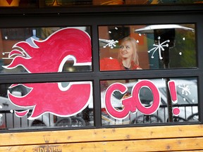 Amanda from Side Street Pub and Grill in Kensington touches up one of their window displays to show their Flames pride in Calgary on Thursday, May 19, 2022.