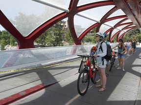 Cyclists and pedestrians look at damage to the Peace Bridge near downtown Calgary on Sunday, July 24, 2022. Multiple panels have been shattered, causing thousands of dollars of damage.
