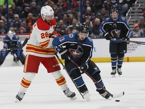 Columbus Blue Jackets' Johnny Gaudreau, right, carries the puck across the blue line past Calgary Flames' Elias Lindholm during the second period of an NHL hockey game Friday, Dec. 9, 2022, in Columbus, Ohio.