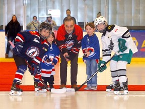 Esso vice-president of public affairs James Kusie, with help from Millie Constable, left, and Esme Baldwin, drop the ceremonial puck between the Northwest Warriors U11 HADP and the Glenlake U11 HADP at the Max Bell Perry Cavanagh arena during the feature game to kick off Esso Minor Hockey week in Calgary on Jan. 13.