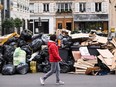 A pedestrian walks past household waste containers in Paris, Sunday, March 12, 2023, which have been piling up since collectors went on strike against the French government's proposed pension reforms a week earlier.
