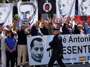 A police officer walks past fascism sympathizers performing the fascist salute and holding banners in the memory of the founder of Falange, Jose Antonio Primo de Rivera, outside the San Isidro cemetery in Madrid, where the fascist politician was buried on April 24, 2023 following his exhumation from the Valle de los Caidos basilica, officially named Valle de Cuelgamuros.