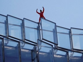 French "Spiderman" Alain Robert waves from atop of the Tour Alto skyscraper in the financial and business district of La Defense, naming his feat "The People", after climbing it in Courbevoie near Paris, France, Wednesday, April 19, 2023.