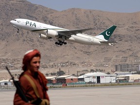 A Taliban fighter stands guard as a Pakistan International Airlines plane takes off with passengers onboard at the airport in Kabul on September 13, 2021.