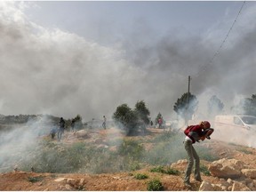 Palestinian protesters rush away from tear gas amid clashes with Israeli security forces during a protest in the village of Beita, south of Nablus in the occupied West Bank, on April 10, 2023, against a march by settlers to the nearby Israeli outpost of Eviatar.
