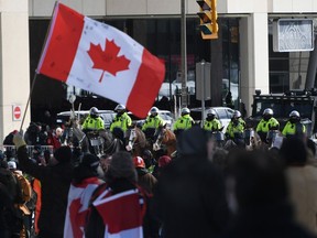 A person waves a Canadian flag as police on horseback and an armoured police vehicle are positioned in front of protesters, on the 22nd day of a protest against COVID-19 measures that has grown into a broader anti-government protest, in Ottawa, Feb. 18, 2022.