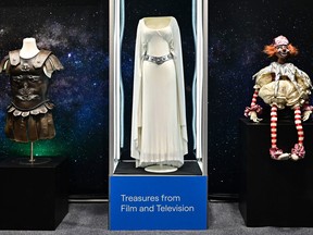 The Princess Leia dress worn by actress Carrie Fisher in the 1977 film "Star Wars" is displayed between the General Maximus dress cuirass worn by Russell Crowe in the 2000 film "Gladiator," (L), and the evil clown doll from the 1982 film "Poltergeist" on May 16, 2023 at Propstore in Valencia, California.