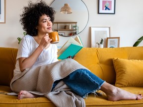 Woman reading a book at home, relaxing, drinking coffee sitting on the couch.