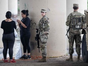 Members of the U.S. military stand near two migrants under a bridge that connects the U.S. and Mexico, as they head to the edge of the Rio Grande river in Eagle Pass, Texas, Wednesday, May 10, 2023.