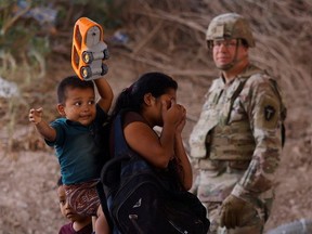 Migrants stand near the Rio Bravo river after crossing the border to, request asylum in the United States, as a member of the Texas Army National Guard stands guard to inhibit migrants crossing, as seen from Ciudad Juarez, Mexico May 13, 2023.