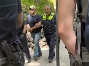 In this image taken from video, a suspect is taken away by two police officers near Neuschwanstein castle in Schwangau, southern Germany, Thursday June 15, 2023. An American man has been arrested after allegedly assaulting two U.S. tourists near Neuschwanstein castle in southern Germany and then pushing them down a steep slope, an attack that left one of the women dead, authorities said Thursday.