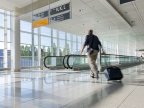 In this file photo, a tourist with baggage walks towards a moving walkway at an airport.