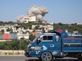 A truck drives on a road as a plume of smoke rises from a building during a reported Russian air strike on Syria's northwestern rebel-held Idlib province, on June 25, 2023. The strikes killed at least 13 people including civilians and children, the deadliest such assault on the war-torn country this year, a war monitor said