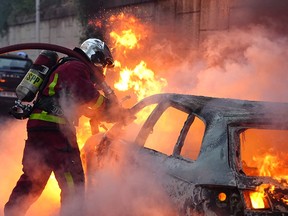 A firefighter works to put out a burning car on the sidelines of a demonstration in Nanterre, west of Paris, on June 27, 2023.
