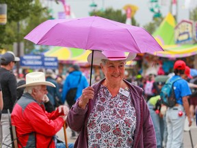 Phyllis Davie shelters from the showers on a cool day at the Calgary Stampede on Tuesday, July 11, 2023.