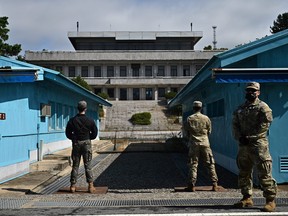 UNC (United Nations Command) soldiers (right) and a South Korean soldier (left) stand guard before North Korea's Panmon Hall (rear centre) and the military demarcation line separating North and South Korea, at Panmunjom, in the Joint Security Area (JSA) of the Demilitarized Zone (DMZ) on Oct. 4, 2022.