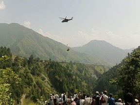 People watch as an army soldier slings down from a helicopter during a rescue mission to recover students stuck in a chairlift in Pashto village of mountainous Khyber Pakhtunkhwa province, on August 22, 2023.