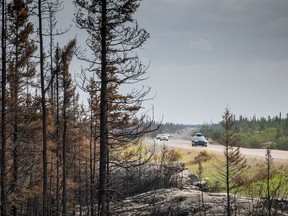 Evacuees from Yellowknife make their way along Highway 3 at the edge of a burned forest on Thursday, Aug. 17, 2023. Northwest Territories officials are using roadblocks to turn back Yellowknife residents who are attempting to return home despite the city still being under a state of emergency.