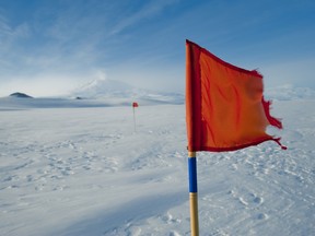 A red flag blows in the wind on the McMurdo Sound Ice Shelf with Mt Erebus, Ross Island in the Background.
