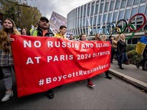 Ukrainians walk past the headquarters of International Olympic Committee (IOC) during a protest against the proposed IOC roadmap to organize the return to competition of Russian athletes under a neutral flag, provided that they have "not actively supported the war in Ukraine" in Lausanne on March 25, 2023.