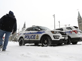 A person passes police officers in their vehicles on Wellington Street in front of Parliament Hill as demonstrators mark the one year anniversary of the Freedom Convoy on Parliament Hill in Ottawa, on Sunday, Jan. 29, 2023.