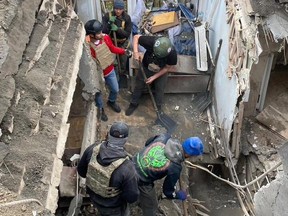 Calgarian Mac Hughes (in green helmet with double patches) shovels debris at a home struck by Russian artillery fire in Kherson, Ukraine earlier this month.