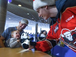 Calgary Hitmen Carson Focht hands a teddy bear to one-year-old Annalia as her father Arlen Wolkowski watches at Alberta Children's Hospital on Monday, December 2, 2019. Some members of the Calgary Hitmen were at the hospital to distribute and deliver the stuffed toys from the ENMAX Teddy Bear Toss 2019.