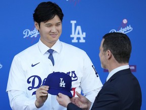 Los Angeles Dodgers' Shohei Ohtani is handed a baseball cap by president of baseball operations Andrew Friedman.