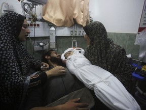 A Palestinian woman shows the body of her grandchild after it was killed in the Israeli bombardment of the Gaza Strip outside a morgue in Rafah, Tuesday, Dec. 19, 2023.
