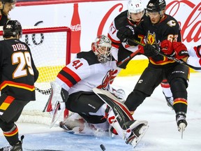 Calgary Flames forward Adam Ruzicka scrambles to reach a loose puck in front of New Jersey Devils goaltender Vitek Vanecek during NHL action in Calgary on Saturday