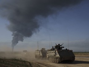 Israeli soldiers move on armoured personnel carriers near the Israeli-Gaza border as smoke rises to the sky in the Gaza Strip, seen from southern Israel, Sunday, Jan. 21, 2024.