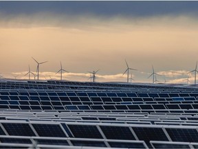 Solar panels at the Travers Solar Project with wind turbines behind them west of Lomond, Alta.