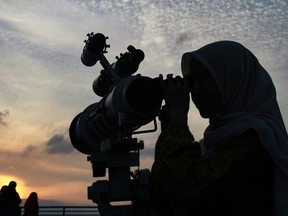 A Muslim woman (R) looks through a telescope for sighting of the new moon at sundown to mark the start of Islam's holy fasting month of Ramadan in Medan on March 10, 2024.